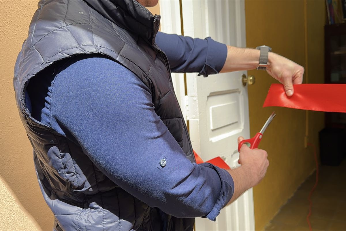 Manos cortando un listón rojo con tijeras, en la puerta de un salón.