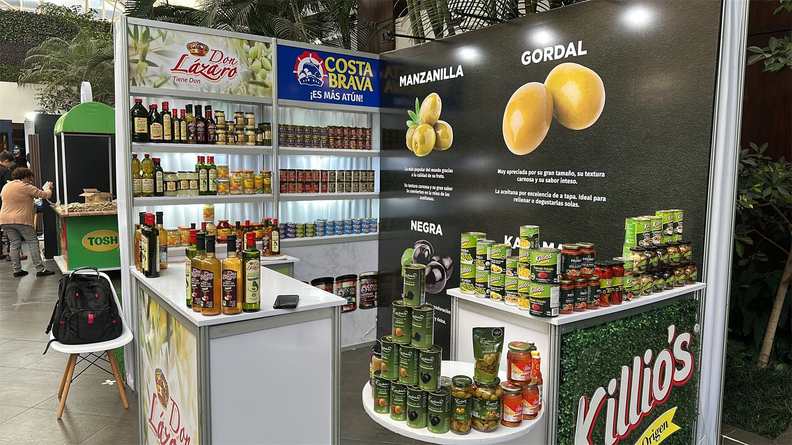 Esquina de exhibición con estantes de Don Lázaro y Costa Brava y una mesa de Killio’s con latas y frascos.