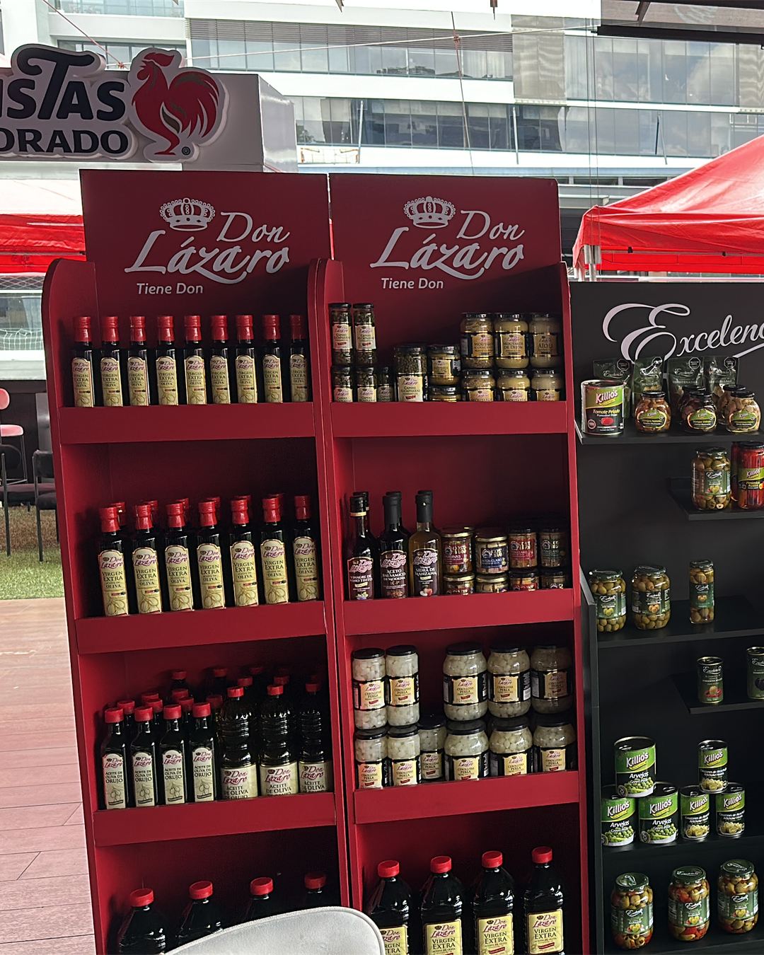 Exhibidores rojos de Don Lázaro en una feria, con aceites y conservas en los estantes.